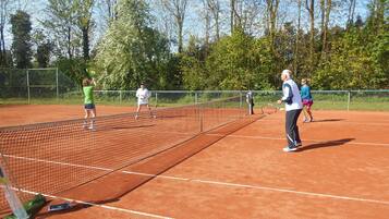 Un court de tennis avec un filet, entouré d’arbres et d’une clôture.