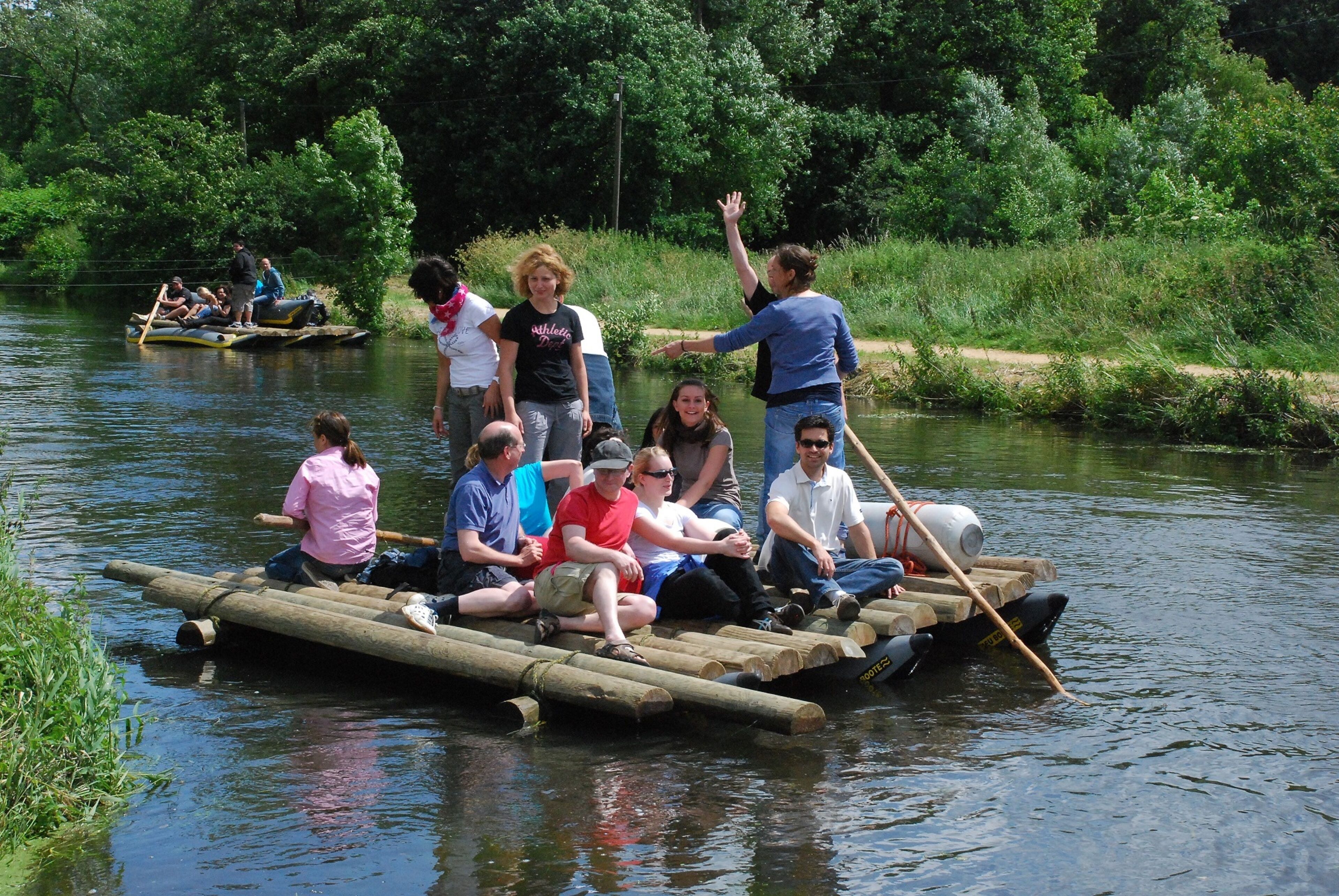 A group of people on a log raft in a river surrounded by greenery.