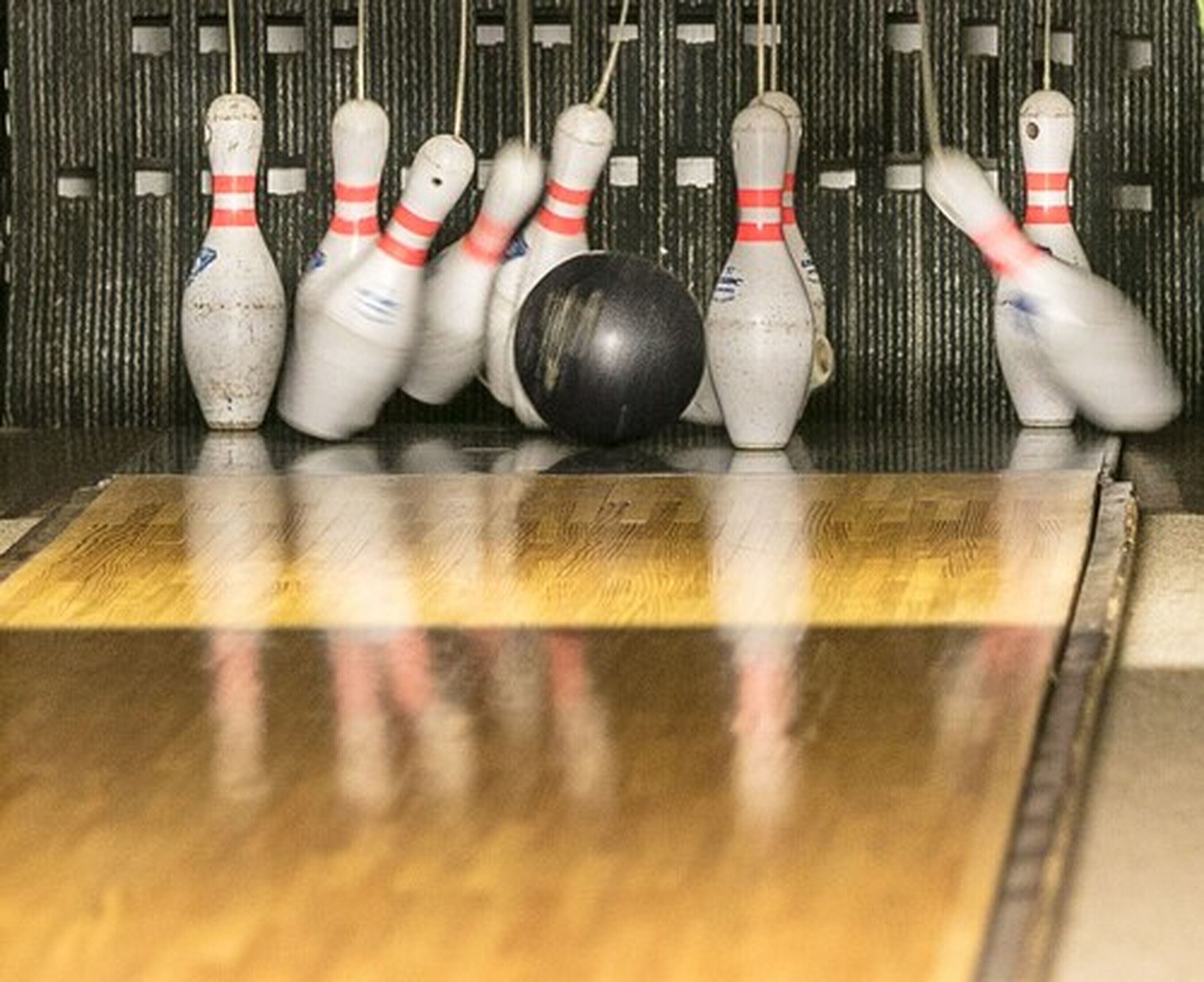 Une salle de bowling dotée d’un plancher en bois et d’un jeu de quilles blanches à rayures rouges.