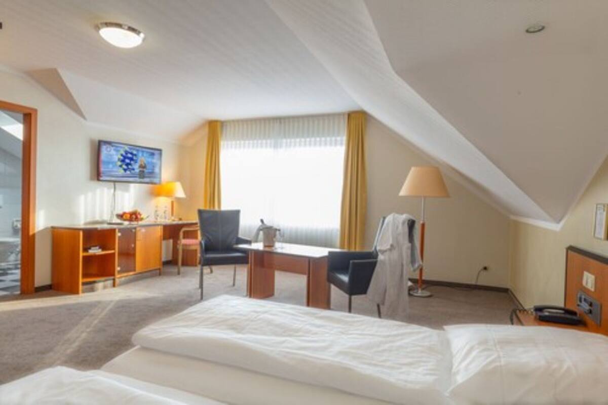 A hotel room with a bed, desk, chair, and a television on the wall.