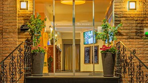 The entrance of Sport-und Tagungshotel De Poort with a brick facade, large glass doors, and potted plants on either side. - Sport - und Tagungshotel De Poort (Goch)