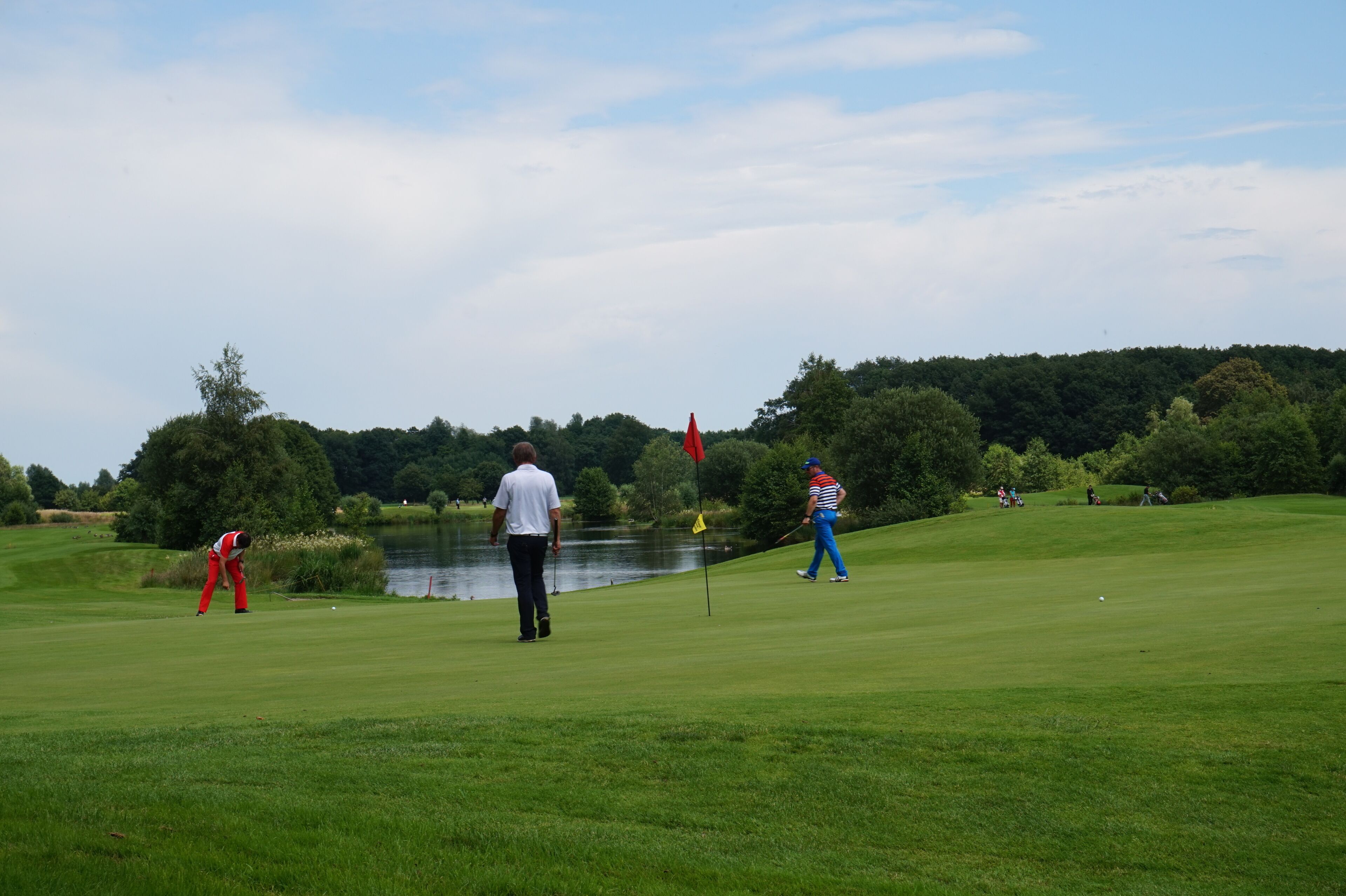 Un campo de golf con un estanque, árboles y una bandera.