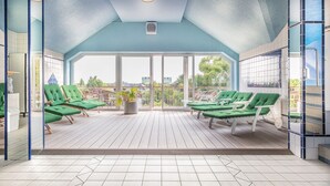 A sunlit outdoor lounge area with green cushioned chairs and a potted plant. - Sport - und Tagungshotel De Poort (Goch)