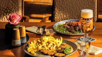 A dining table with a plate of food, a glass of beer, and a vase with a rose.