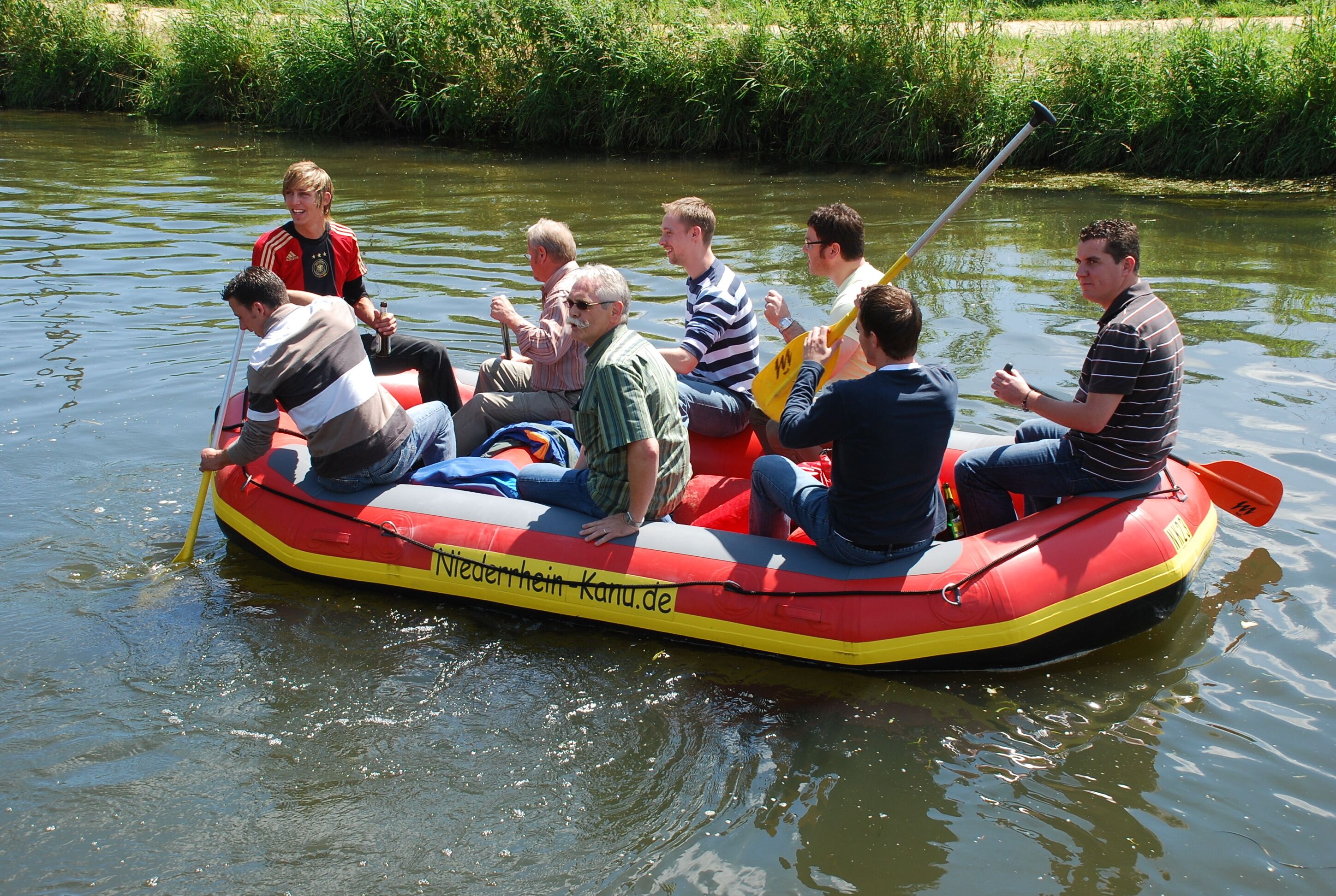 Un groupe de personnes se trouve dans un radeau gonflable rouge et jaune sur une rivière paisible.
