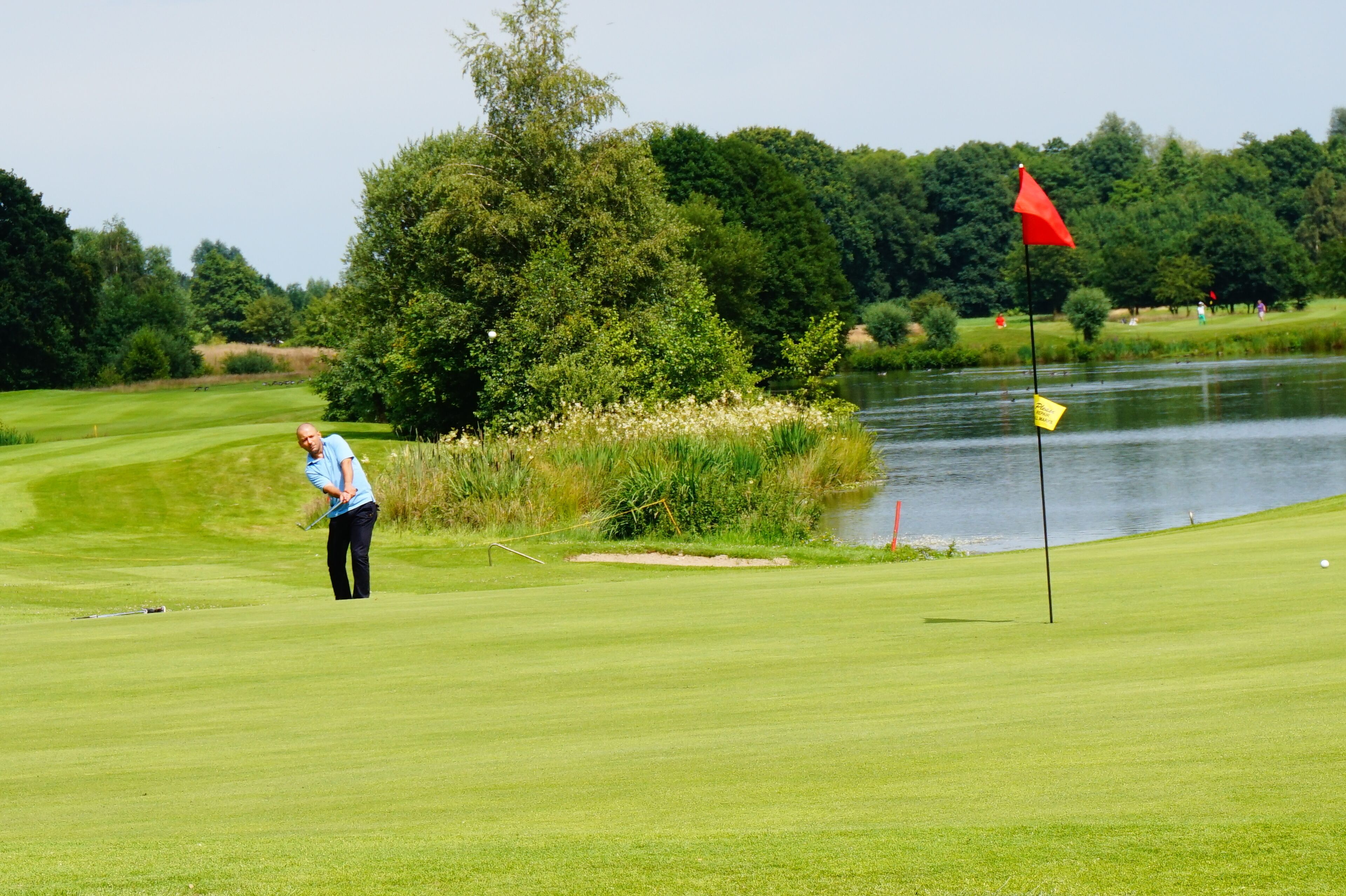 En golfbane med et vandhazard og et rødt flag, der markerer hullet.