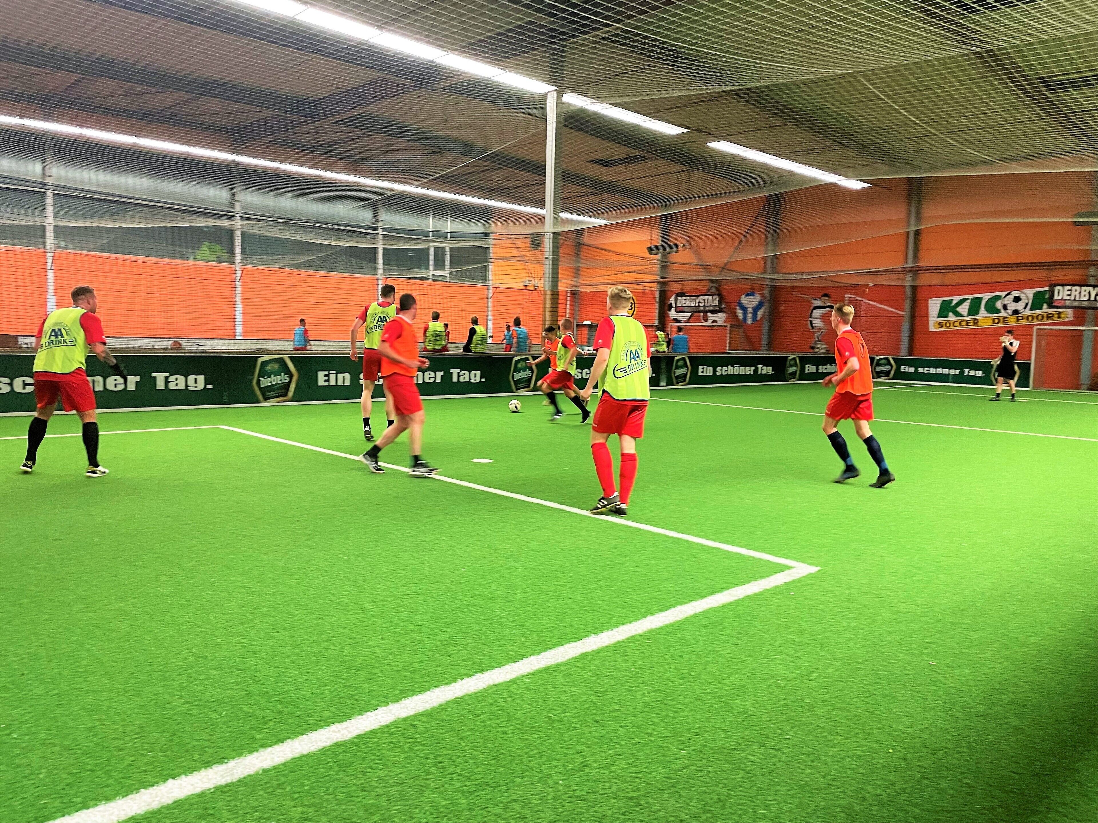 Una cancha de fútbol cubierta con césped artificial, rodeada de asientos naranja y publicidad.