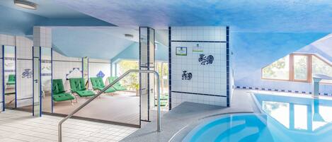 A swimming pool area with green lounge chairs, a tiled wall with a logo, and a clear view of the sky.