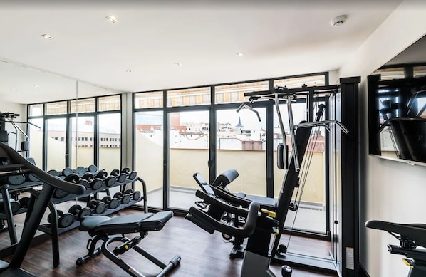 A gym with exercise equipment, large windows, and a view of buildings outside.