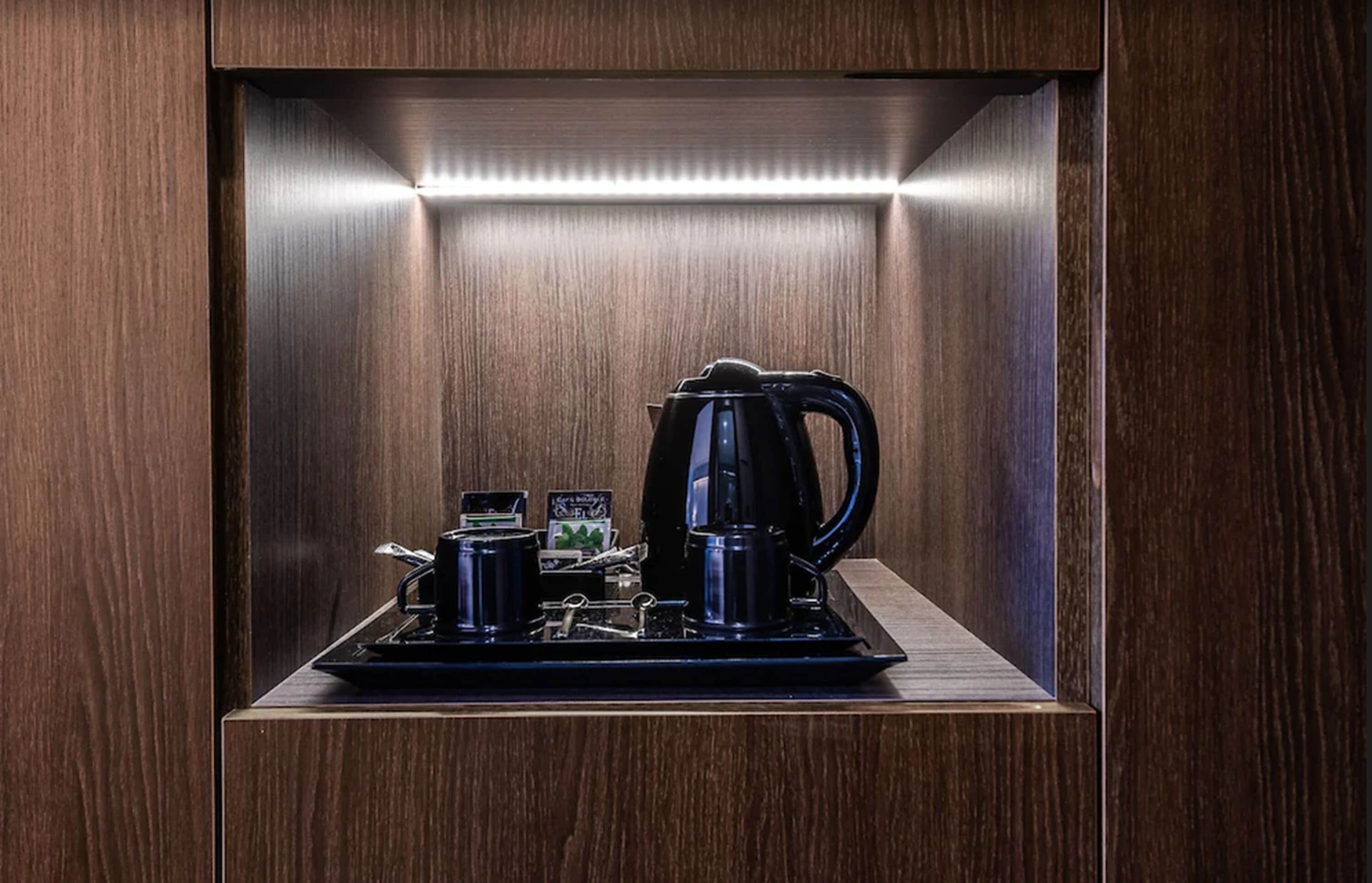 Une pièce compacte et bien éclairée, avec un décor de panneaux en bois, comprenant un coin café équipé d’une bouilloire, de tasses et d’un petit plateau.