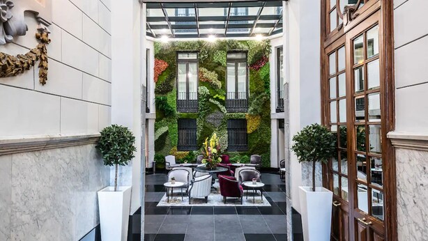 Un vestíbulo con jardín vertical verde, suelo de mármol y mobiliario clásico.