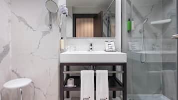 Une salle de bain moderne avec un pare-baignoire en marbre, un lavabo blanc, une douche en verre et un petit tabouret.