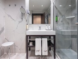 Ein modernes Badezimmer mit Marmor-Spritzschutz, einem weißen Waschbecken, einer Glasdusche und einem kleinen Hocker.