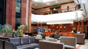 En rummelig lobby med flere siddeområder, en receptionsdisk og en altan i anden etage med gelænder.