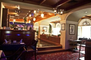 A restaurant with a bar area, wooden ceiling, and a red patterned carpet.