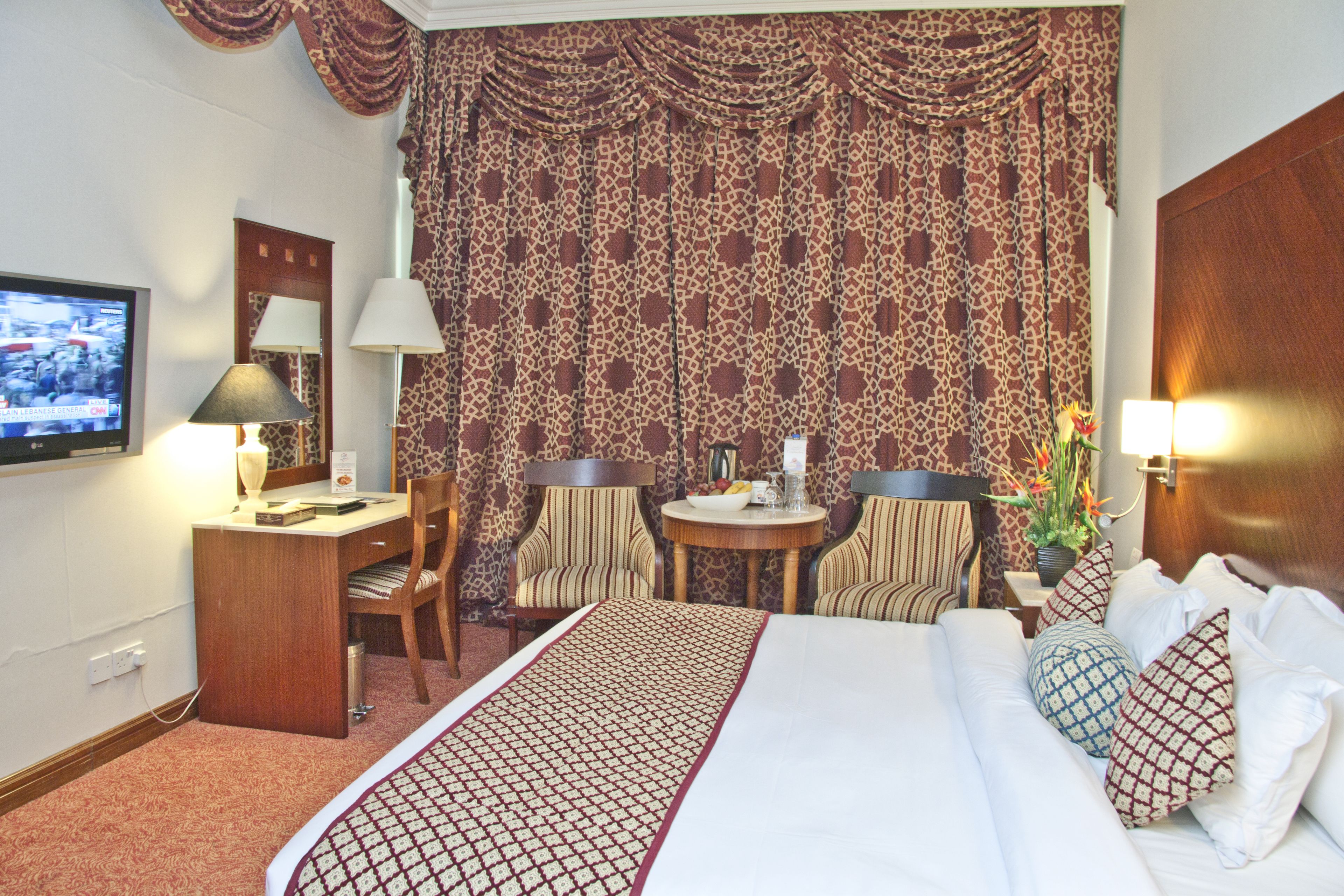 A hotel room with a bed, two chairs, a desk, a TV, and a large patterned curtain.