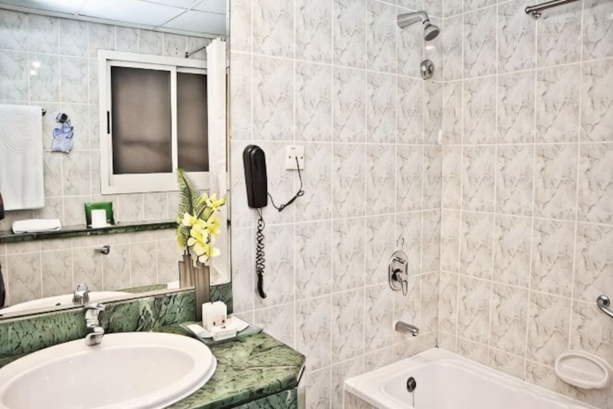 A bathroom with a marble sink, a mirror, a shower, and a telephone.