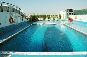 A rooftop swimming pool with clear blue water, lounge chairs, and safety equipment.
