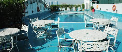 A rooftop pool area with white metal tables and chairs, surrounded by a blue tiled deck.