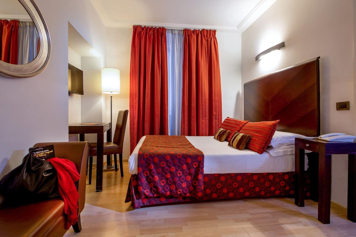 Ein Hotelzimmer mit Bett, Schreibtisch, Stuhl, Lampe und Spiegel.