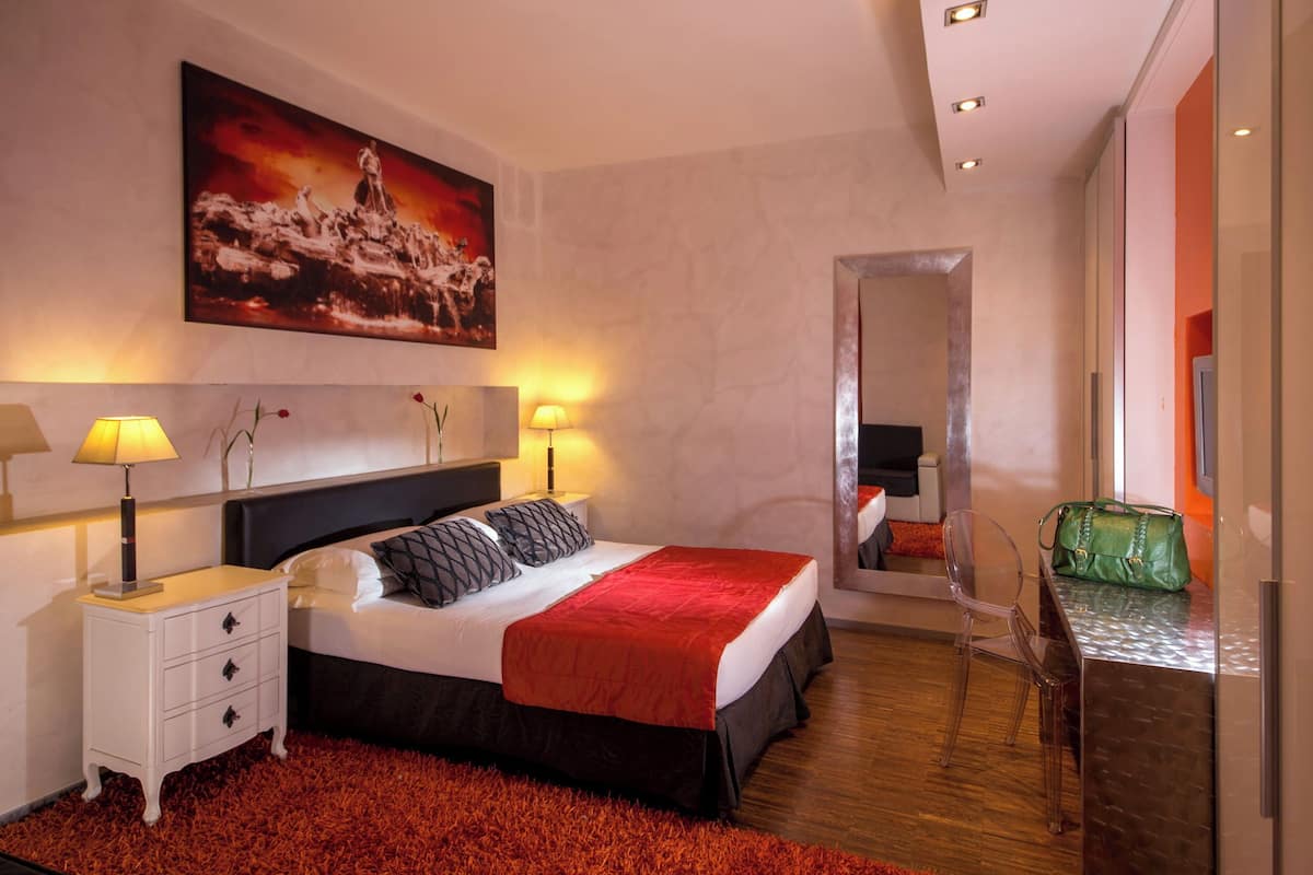 Ein modernes Hotelzimmer mit einem großen Bett, Nachttischlampen, einem roten Teppich, einer grünen Handtasche und einem Bild an der Wand.