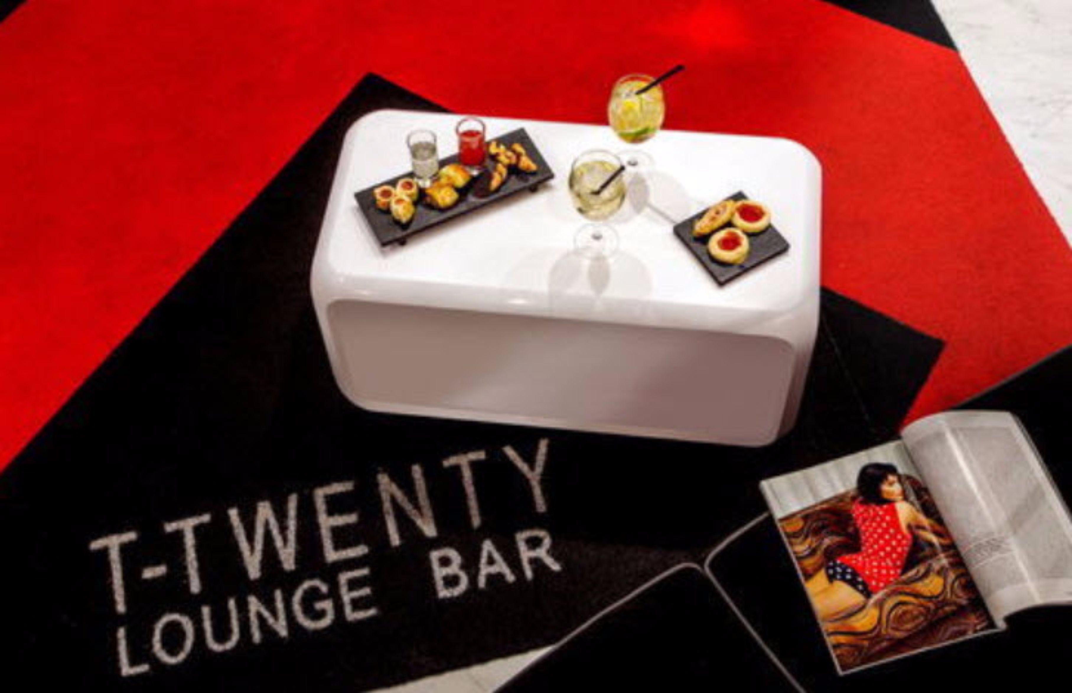 Un comptoir de bar blanc, surmonté d’un set de table noir portant l’inscription « T-TWENTY LOUNGE BAR », et une carte proposant diverses boissons et collations.