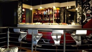 Zona de bar con mostrador, taburetes y una selección de botellas.