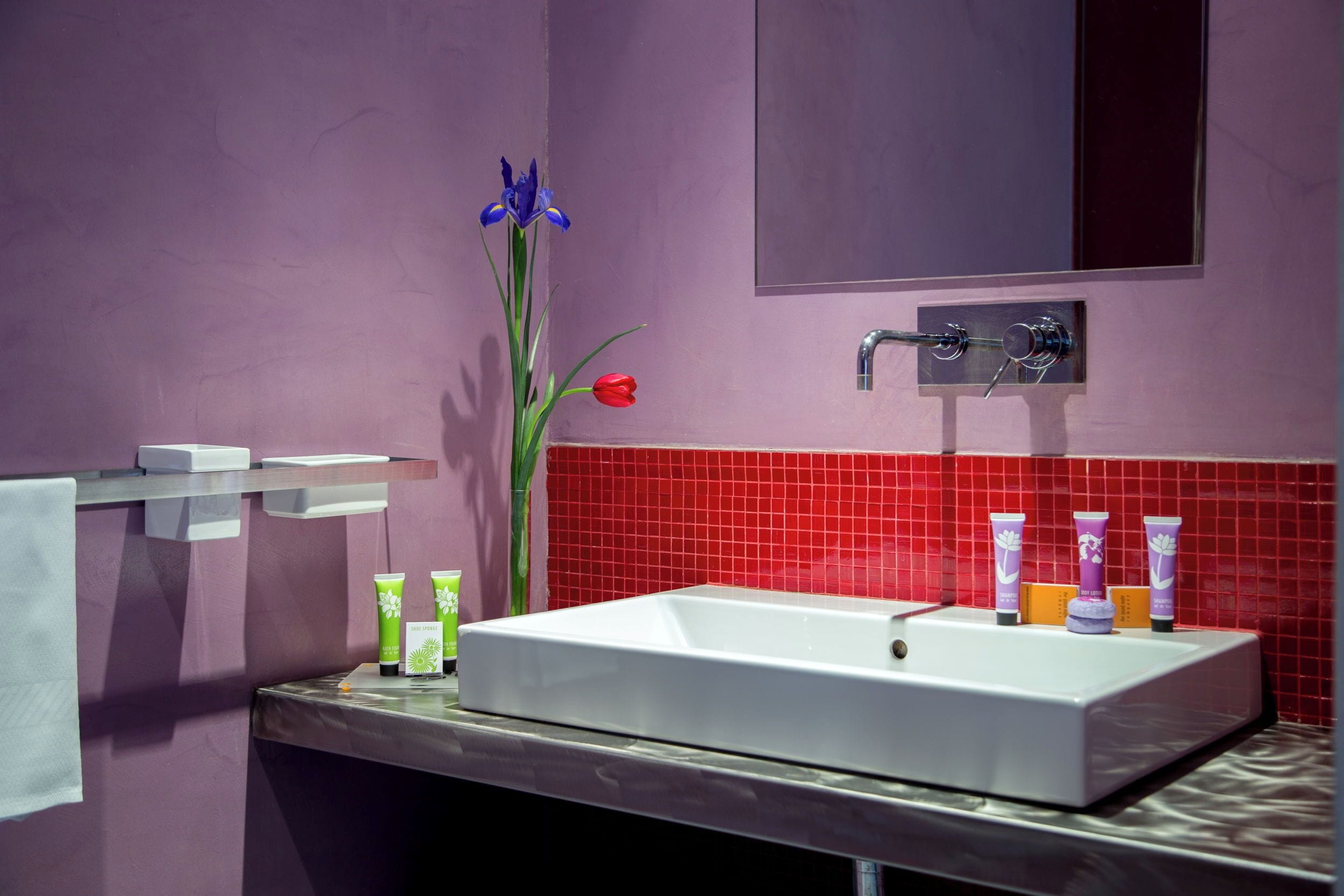 A bathroom with a white sink, purple walls, red tiles, a mirror, and toiletries.