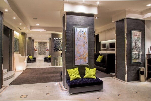 A modern lobby with a central seating area, a reception desk, and a large abstract artwork on the wall. - Hotel Ariston (Rome)