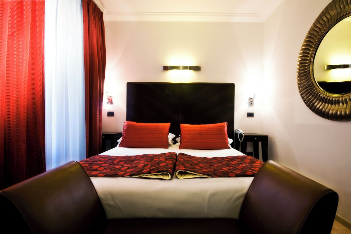Ein Hotelzimmer mit einem großen Bett, roten Kissen, einem mit Beleuchtung versehenen Kopfteil, einem Spiegel und einem roten Vorhang.