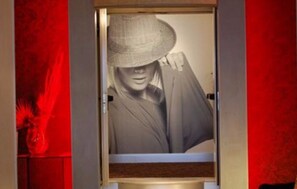 A room with a large poster of a person wearing a hat, a red wall, and a door. - Hotel Ariston (Rome)