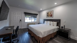 A hotel room with a bed, desk, chair, and a window with a view of the street. - Monterey Surf Inn (Monterey)