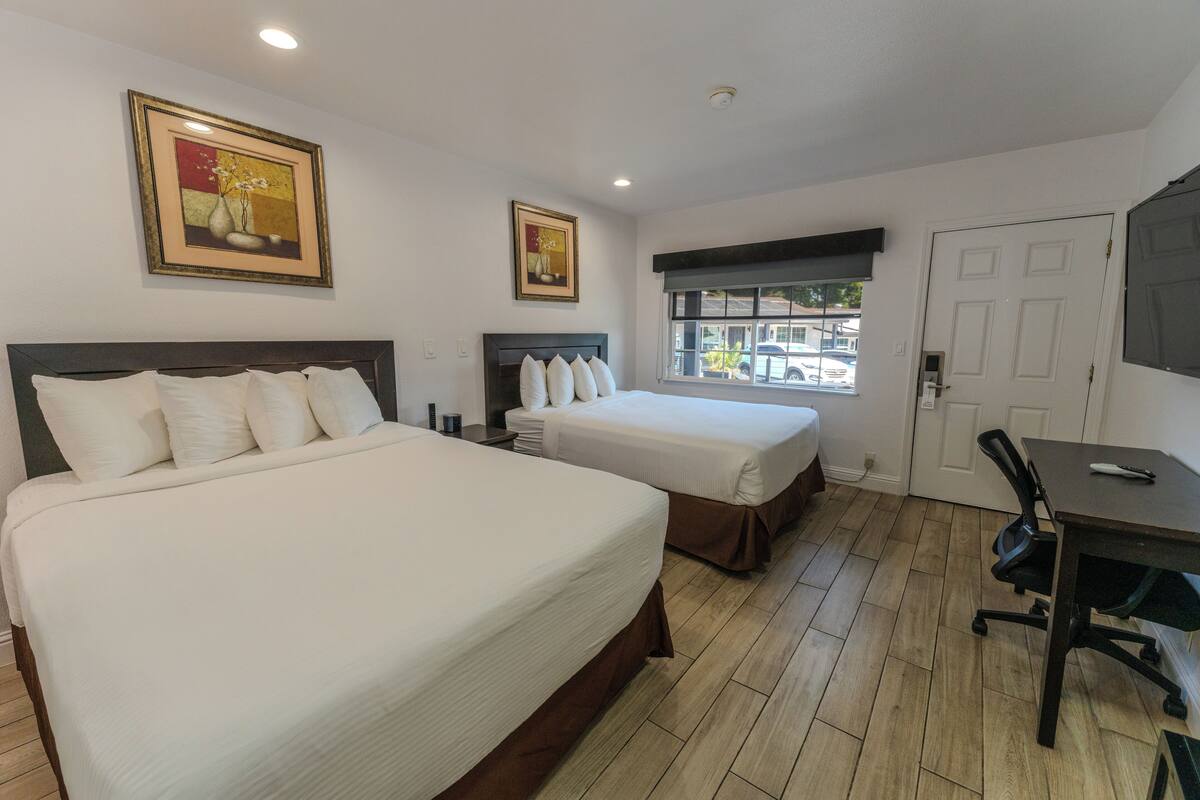 Habitación de hotel con dos camas, un escritorio y ventana con vista a la calle.