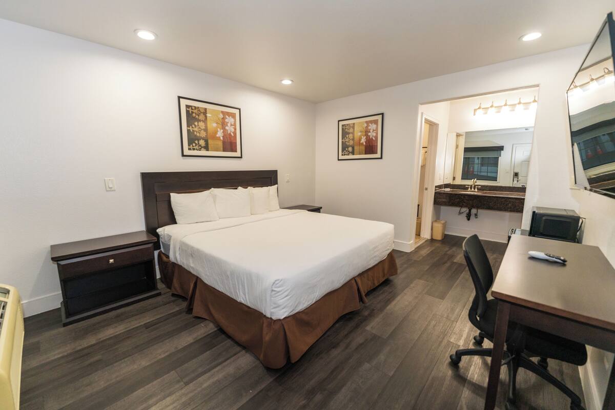Habitación de hotel con una cama grande, un escritorio, una silla, una tocador con espejo y dos cuadros en la pared.
