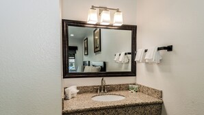 A bathroom with a granite countertop sink, a mirror with lights, and a towel rack. - Monterey Surf Inn (Monterey)