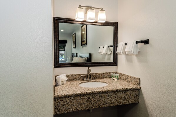A bathroom with a granite countertop sink, a mirror with lights, and a towel rack.
