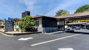 A hotel entrance with a sign for Monterey Surf Inn, a parking lot with directional arrows, and a building with a stone facade. - Monterey Surf Inn (Monterey)