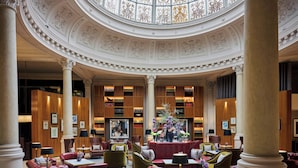 Un amplio vestíbulo con columnas decorativas, un arreglo floral central y una biblioteca con estanterías.