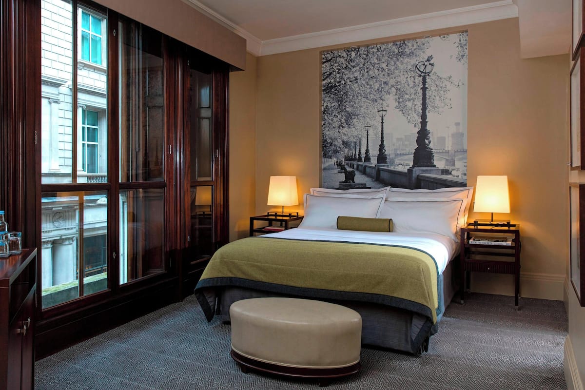 Hotelkamer met een groot bed, twee bedlampen, een raam met uitzicht op gebouwen, en een groot stadslandschap op de muur.