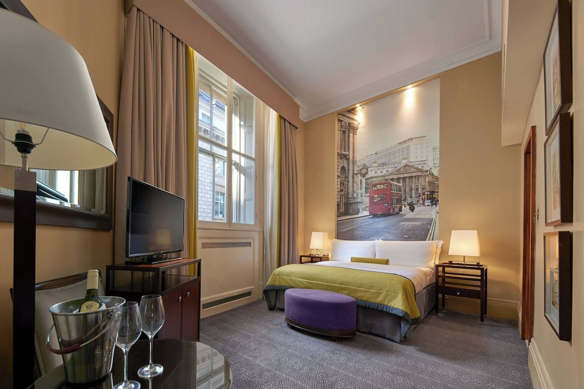 Een hotelkamer met een bed, een televisie, een tafel met champagne en een schilderij aan de muur.
