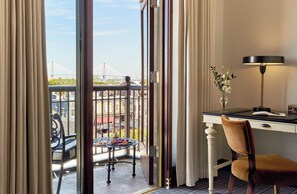 A hotel room with a balcony, a desk, a chair, and a lamp.
