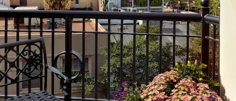 A balcony with a table set for a meal, a potted plant with flowers, and a view of a tower with a clock.