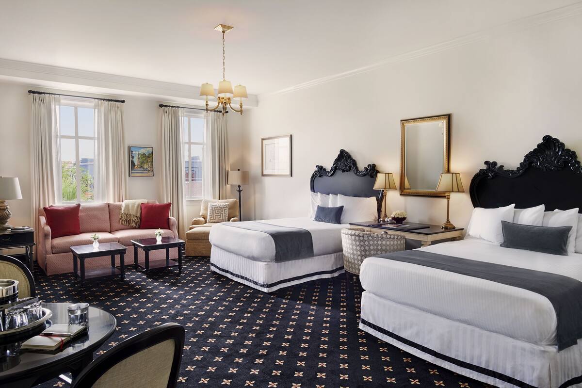 A hotel room with a sofa, two single beds, a dining table, and a chandelier.