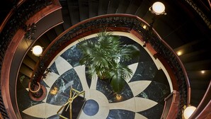 Una imponente escalera con un suelo circular de mármol, una palmera y un candelabro.