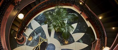 A grand staircase with a circular marble floor, a palm tree, and a chandelier.