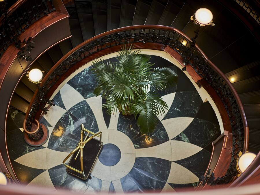 Uma escadaria imponente com piso de mármore circular, uma palmeira e um lustre.