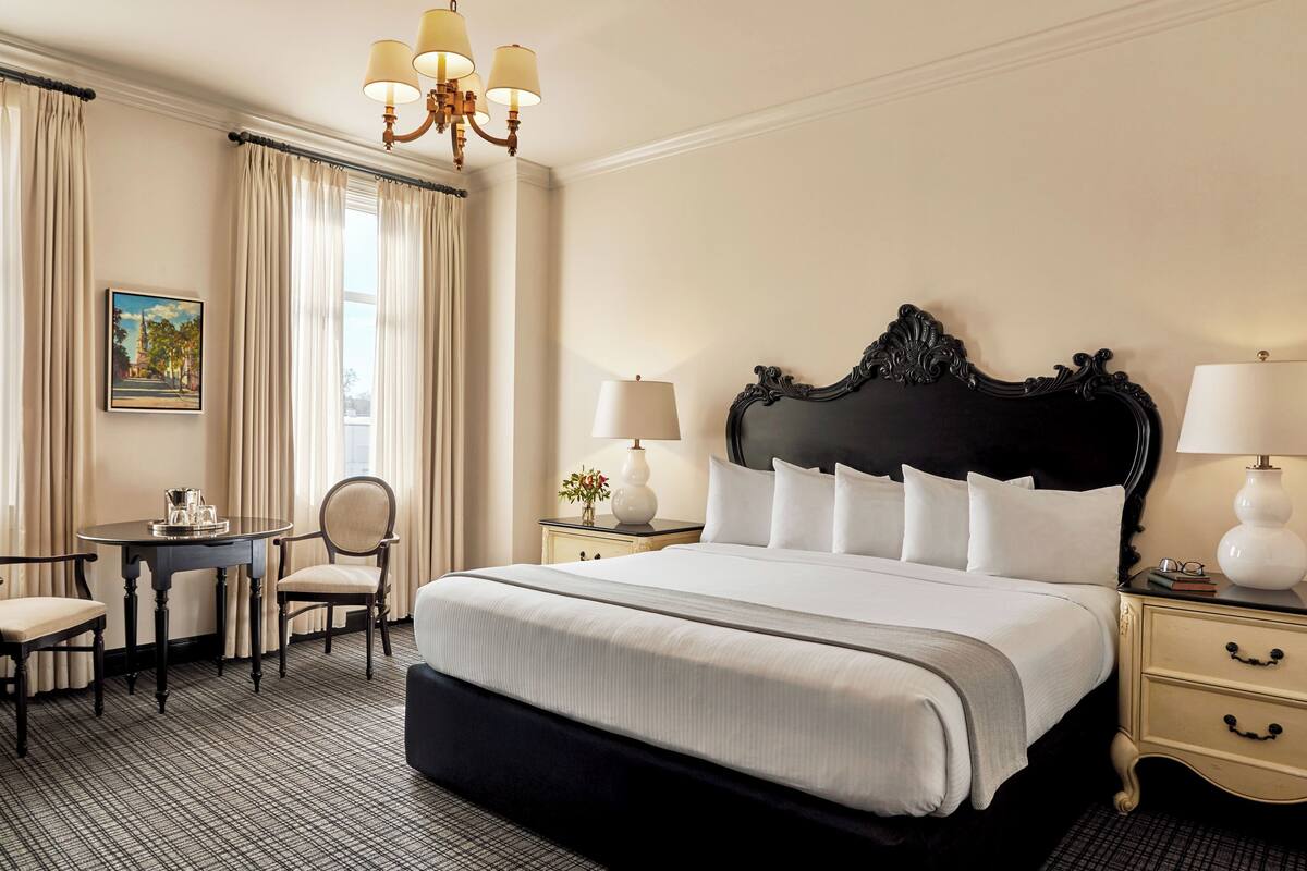 A hotel room with a large bed, two bedside tables, a desk with chairs, and a chandelier.