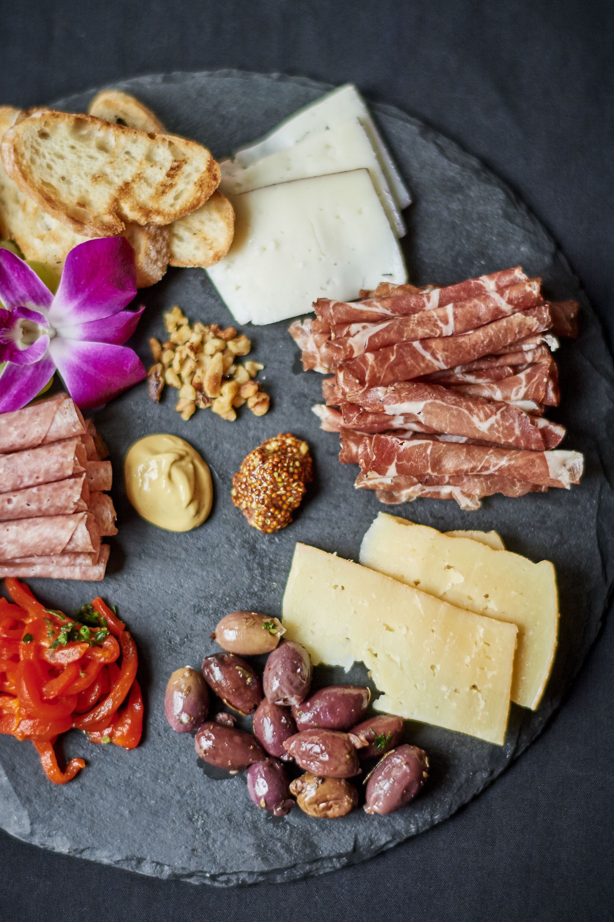 A charcuterie board with various cheeses, meats, nuts, olives, and bread.