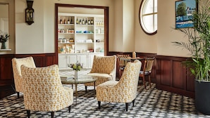 Una habitación con sillas estampadas, una mesa central, una estantería y un ventanal grande.