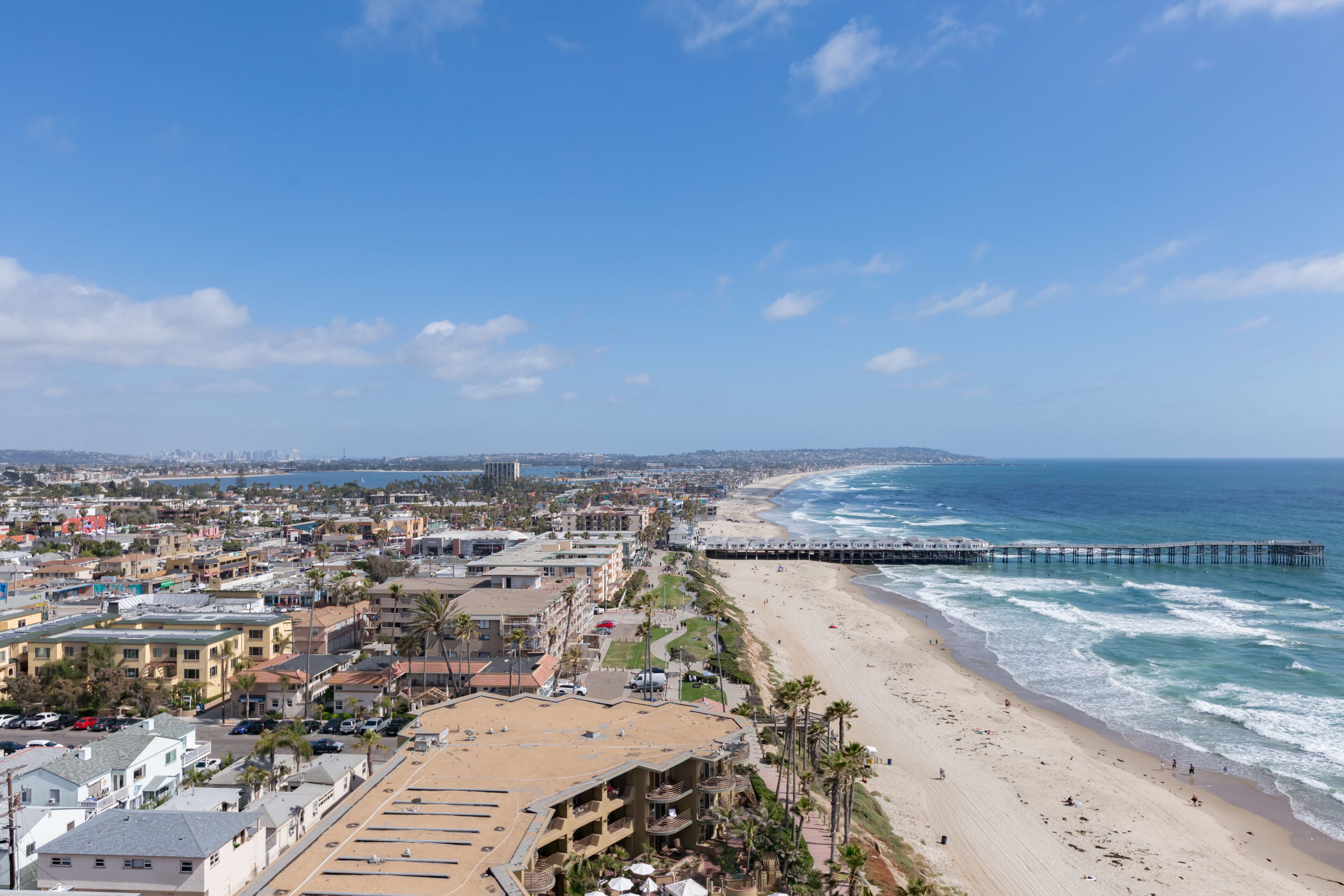 A coastal cityscape with a beach, a pier, and buildings along the shore.